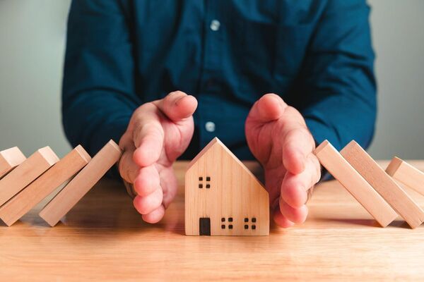 Hands gently protecting a small model house