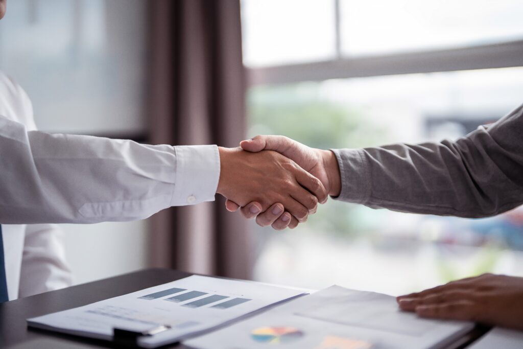 Two business professionals shaking hands over financial documents after signing a deal