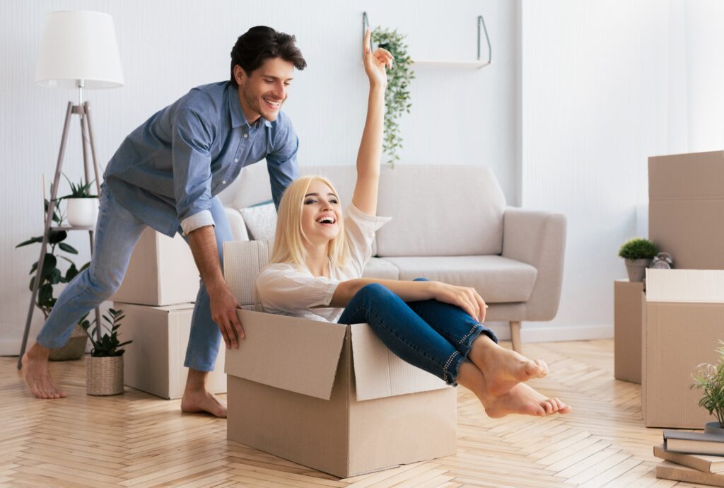Happy woman sitting inside a moving box surrounded by packed boxes in her new home