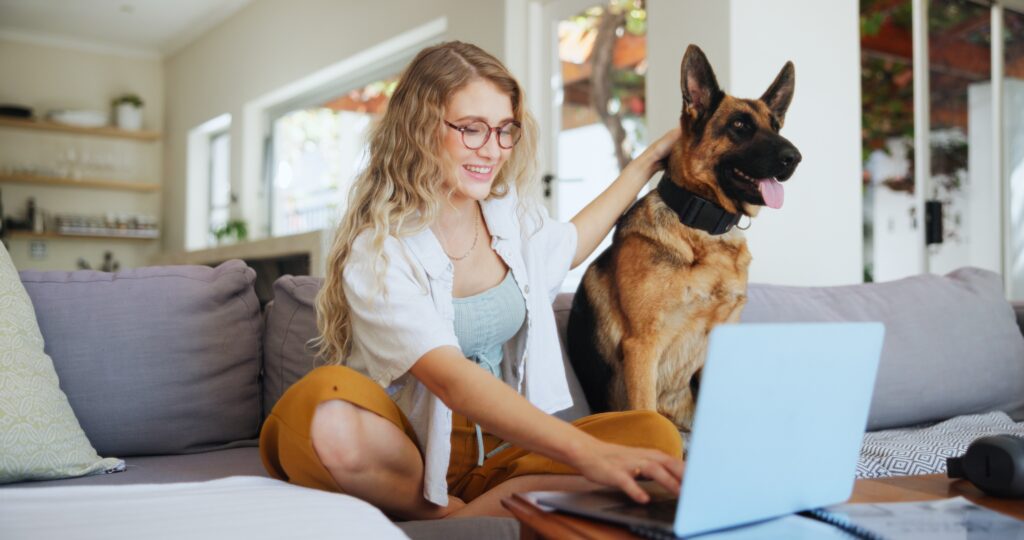 Woman relaxing on a sofa with her dog while using a laptop computer