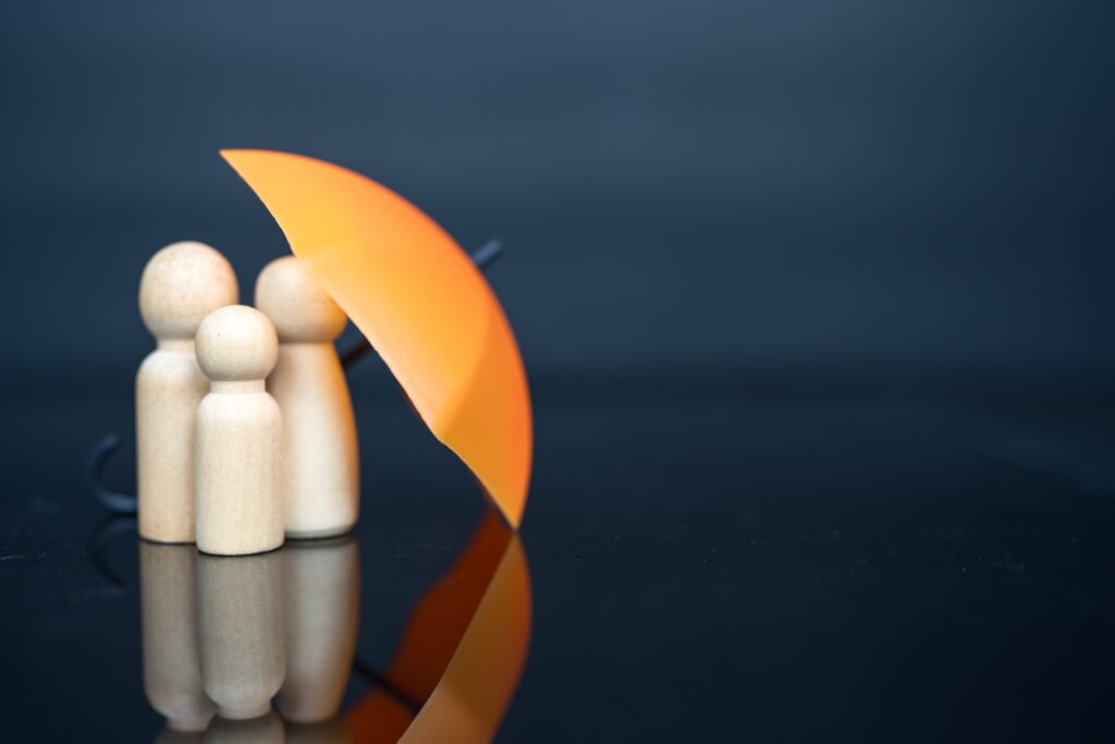 Three wooden family peg dolls sheltered under an orange umbrella against a dark blue background