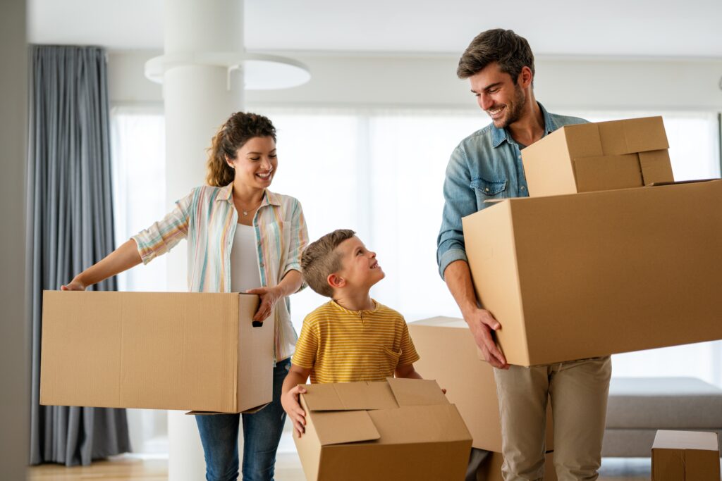 Happy family with a young child carrying moving boxes into their bright new home