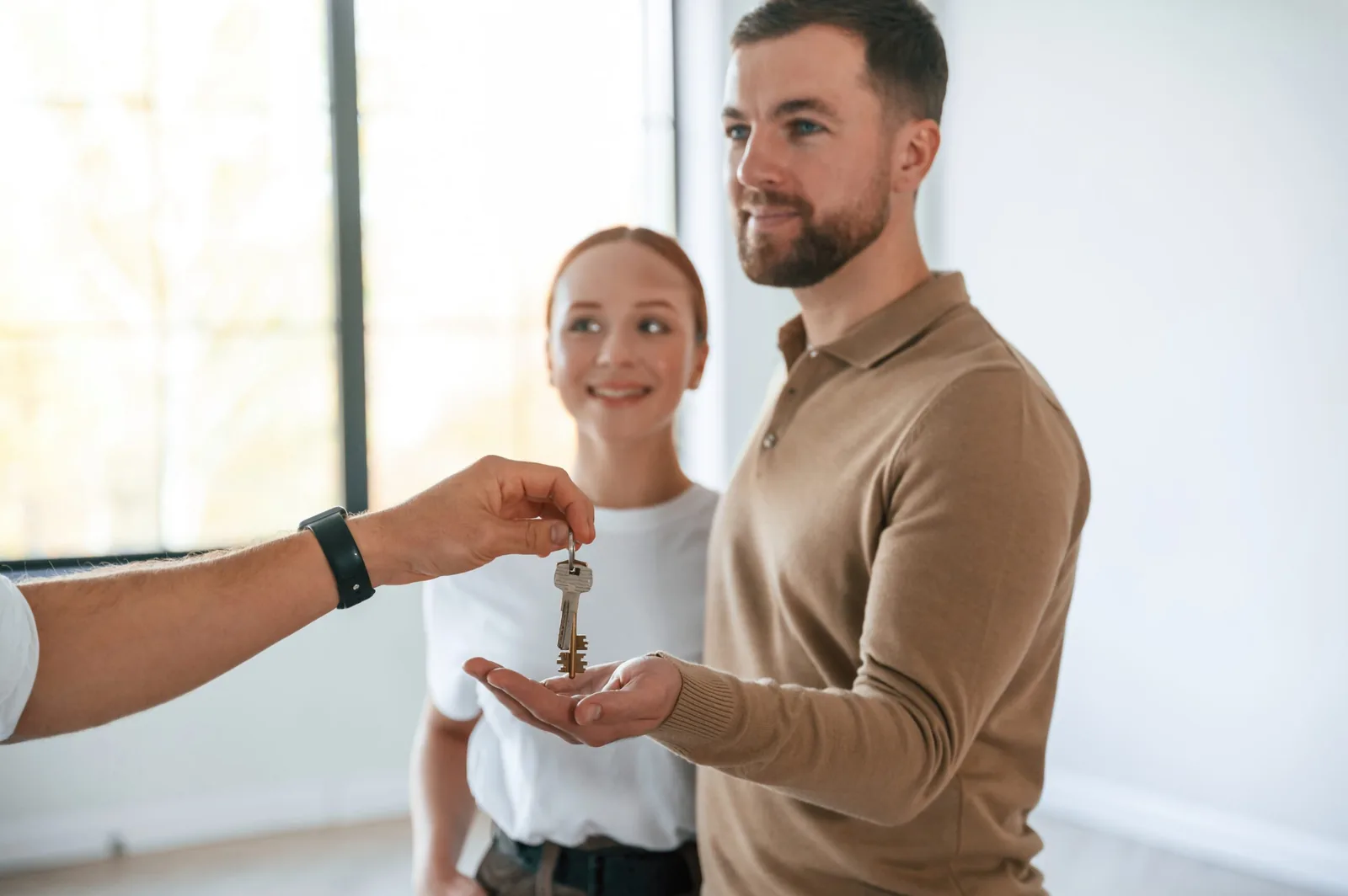 Estate agent handing house keys to a smiling young couple in their new empty home