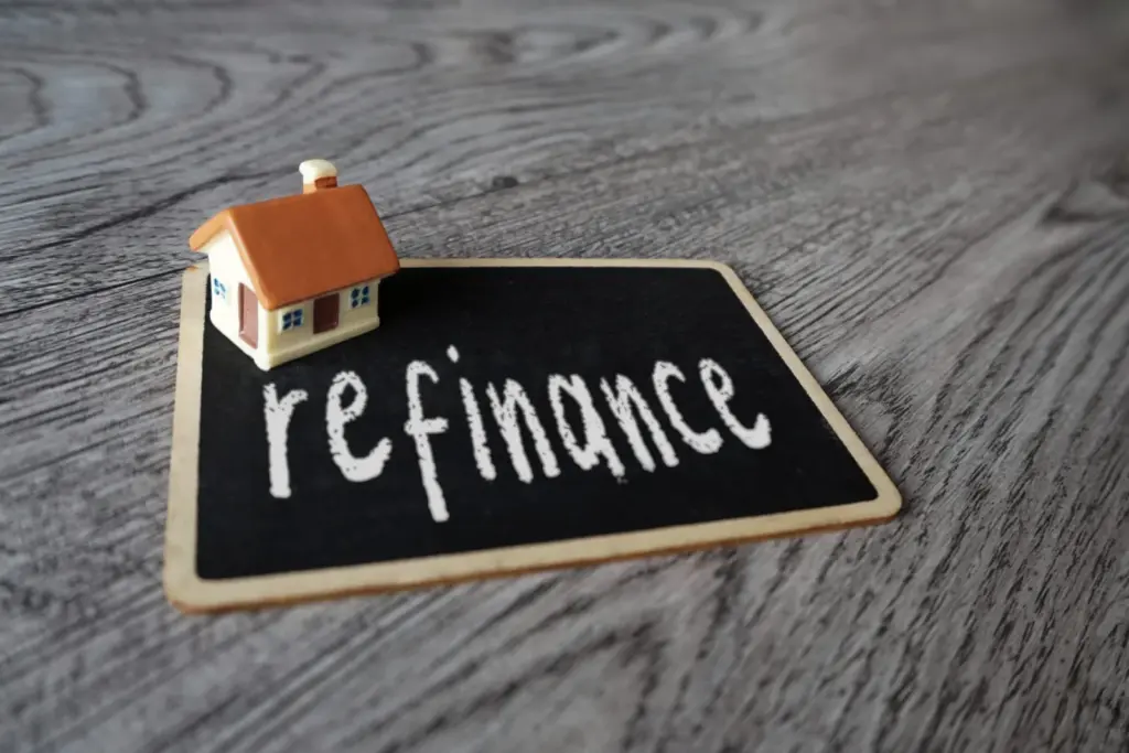 Small wooden house figure beside a chalkboard with the word refinance written in chalk