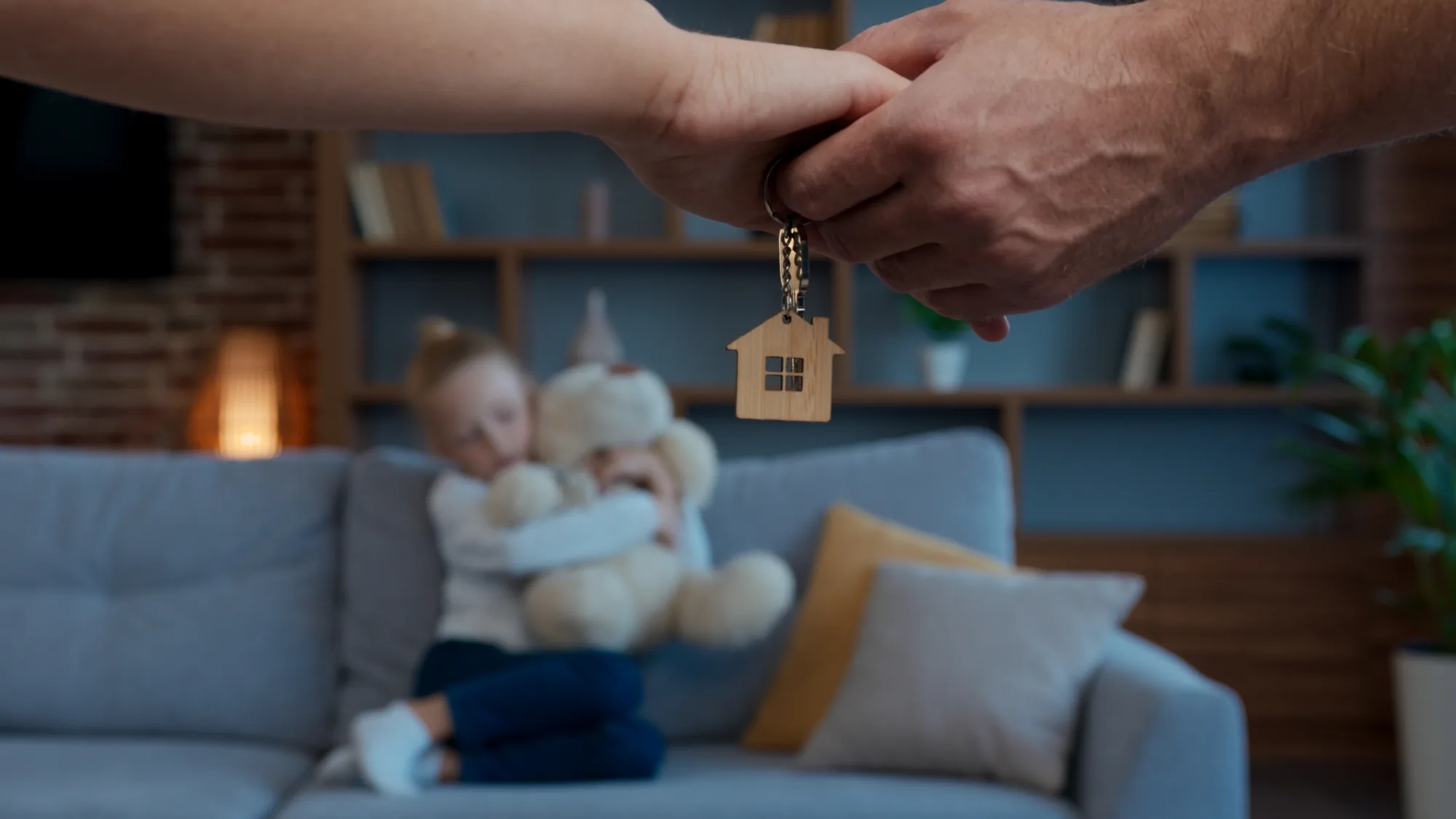 Two people shaking hands over a house keyring while a child sits on the sofa behind