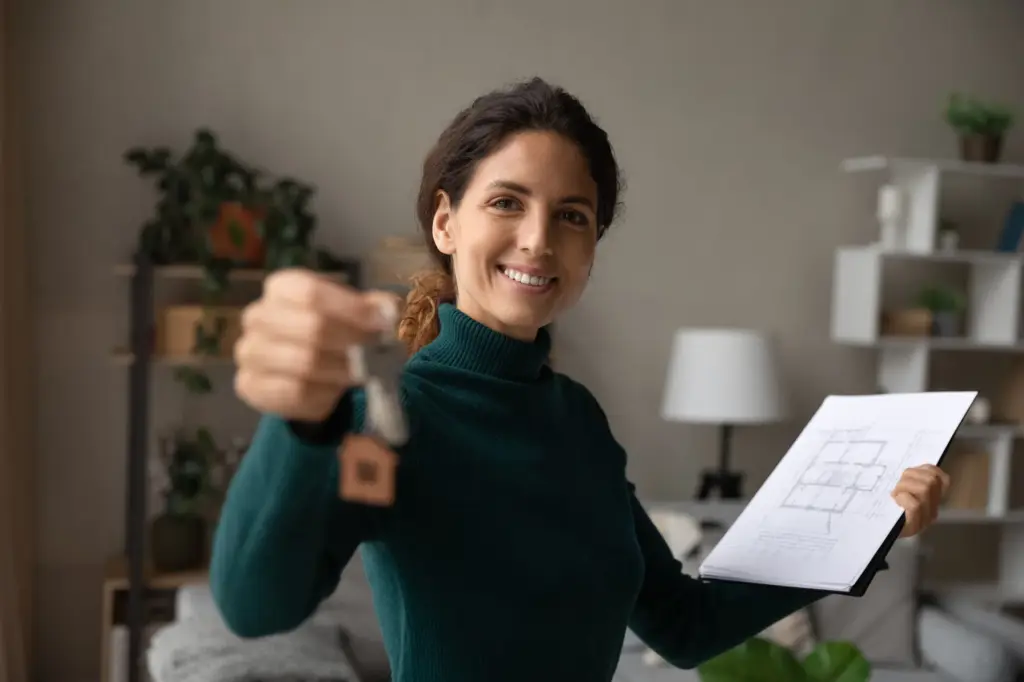 New homeowner holding house keys and floor plans in her living room